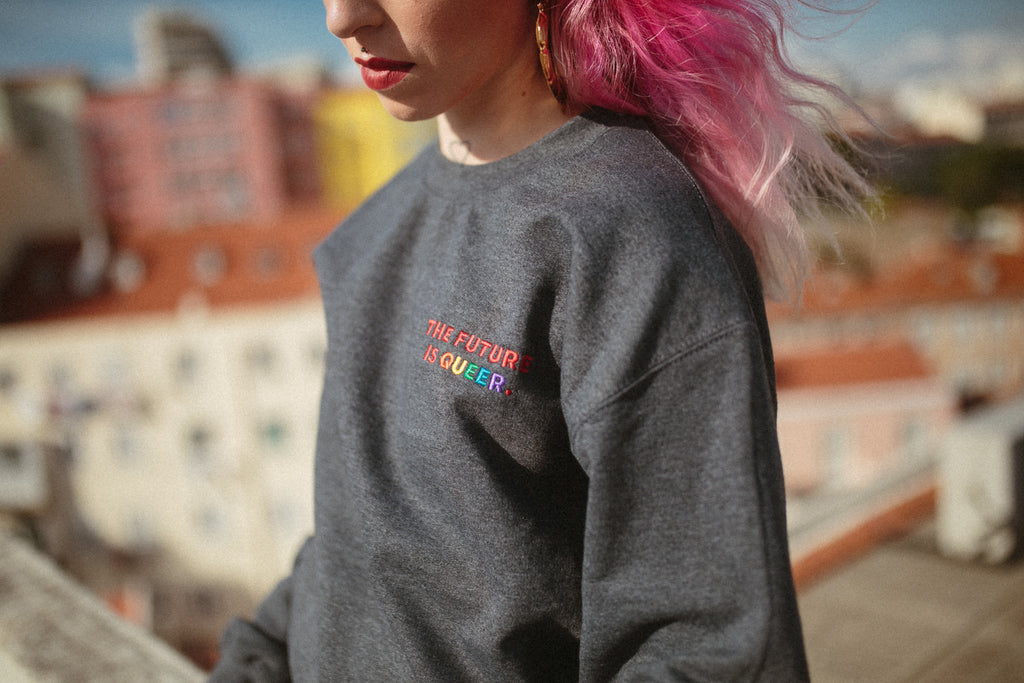A girl with pink hair is wearing the future is queer sweatshirt. 
